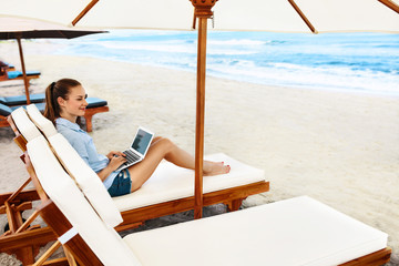 Beautiful Business Woman Working Online On Laptop Computer While Lying On Beach Lounger. Happy Smiling Freelancer Girl Relaxing And Using Notebook For Freelance Internet Work. Communication Technology