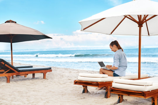 Beautiful Business Woman Working Online On Laptop Computer While Lying On Beach Lounger. Happy Smiling Freelancer Girl Relaxing And Using Notebook For Freelance Internet Work. Communication Technology
