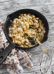 Oat apple crumble in a frying pan on rustic light wood background