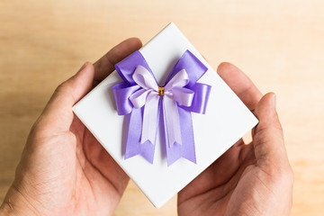 Purple ribbon bow and white gift box on wooden background.