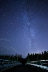 Deurstickers Een nachtelijke hemel vol sterren en zichtbare melkweg met een brug op de voorgrond. Weg die leidt naar donker bos. © Teemu Tretjakov
