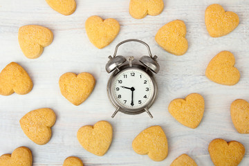 silver wind-up alarm clock near the pile of cookies on a wooden table