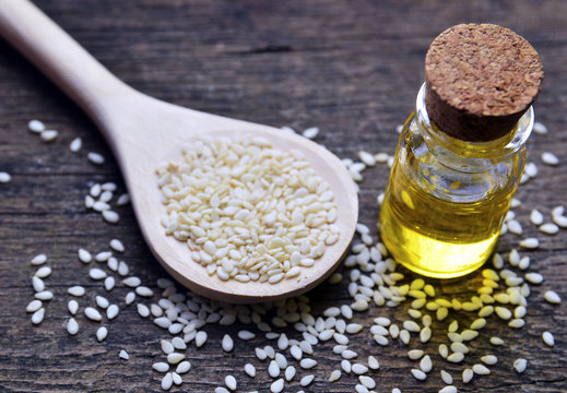 Sesame seeds on wooden spoon and sesame oil in glass jar on wooden background. Selective focus