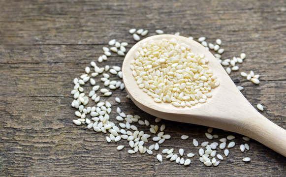 Sesame seeds on wooden spoon on old wooden background. 