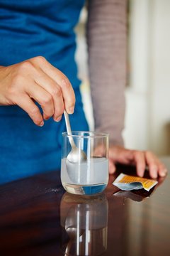 Young woman mixing water-soluble medication from sachet, in glass of water