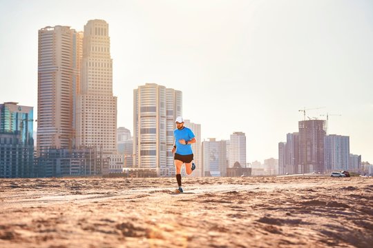 Mid adult man running on sand by skyscrapers, Dubai, United Arab Emirates