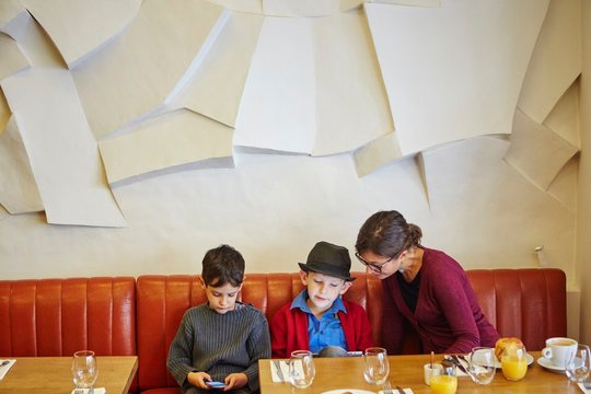 Mother and sons using digital tablet and smartphone in restaurant