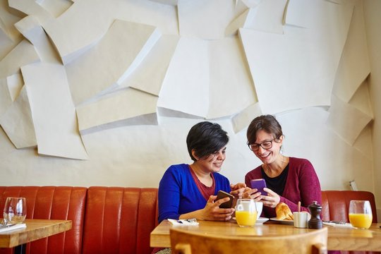 Two adult female friends reading smartphone text in restaurant