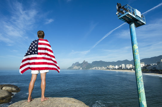 Athlete draped in American flag standing at Arpoador with a view of Rio de Janeiro skyline with Ipanema Beach and Two Brothers Mountain