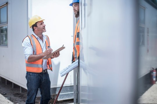 Construction worker talking to foreman from doorway of construction cabin