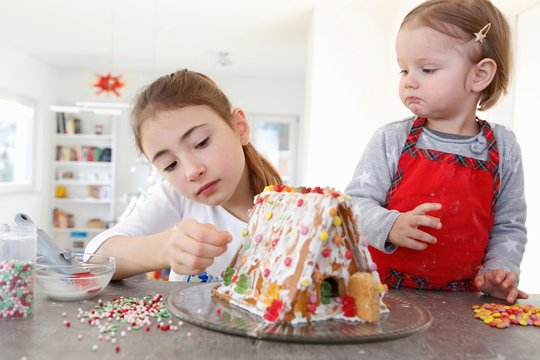 Sisters at kitchen counter decorating ginger bread house