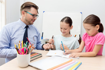 Naklejka premium Smiling young teacher gives pencil to schoolgirl