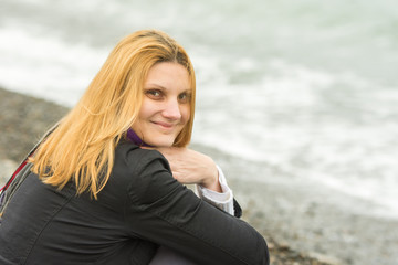 Fototapeta na wymiar Portrait of sitting on the beach smiling young woman in cold weather