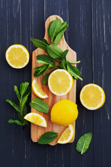 Lemon and mint leaves served on wooden kitchen board on black rustic table, ingredient for summer...