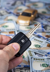 Male hand with car key on the background of dollar bills