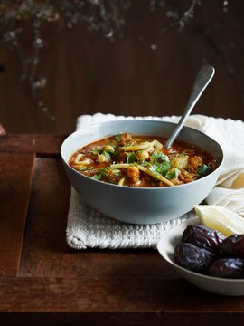 Harira soup in bowl with dates and lemon wedge