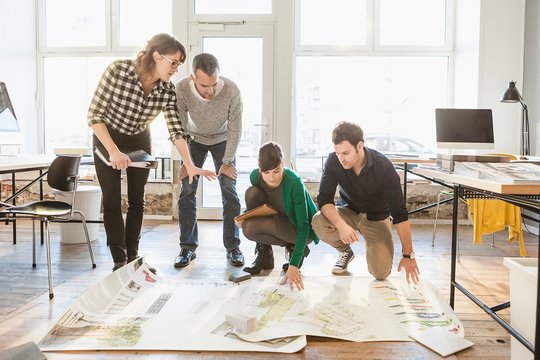 Architects discussing blueprints on wooden floor