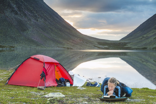 Female hiker reading book while lying near lake