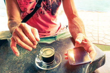 Man hands stirring coffee and holding smart phone at beach bar cafe restaurant - Concept of...