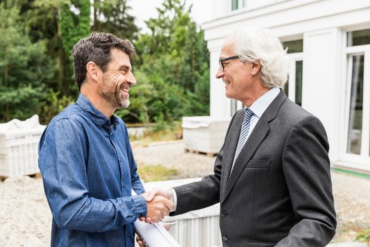 Builder and architect on construction site shaking hands smiling