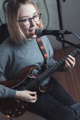 Young woman playing electric guitar and singing to the microphone