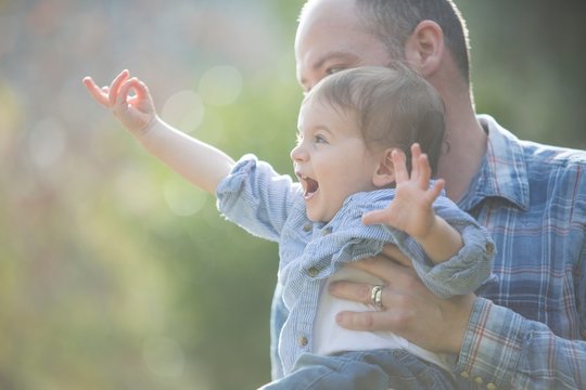 Side view of baby boy being held by father, pointing excitedly