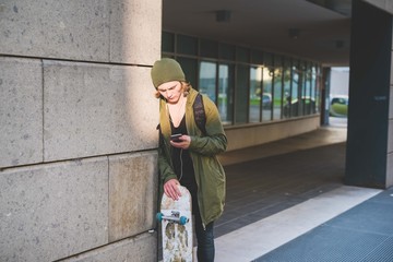 Young male urban skateboarder leaning against wall reading smartphone texts