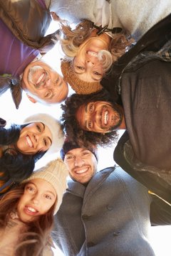 Multi generational family in a huddle bending forward looking down at camera smiling