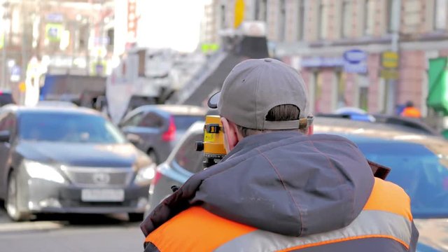 Engineers use tacheometer or theodolite for survey line in city centre, on a background of road works