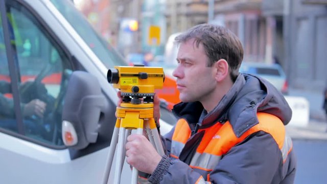 Engineers use tacheometer or theodolite for survey line in city centre, on a background of road works
