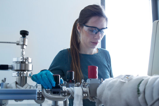 Woman in workshop wearing safety goggles adjusting machine