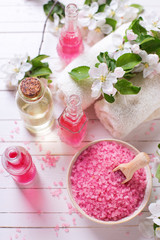 Pink sea salt in bowl, bottles with aroma oil, towels  and flowe