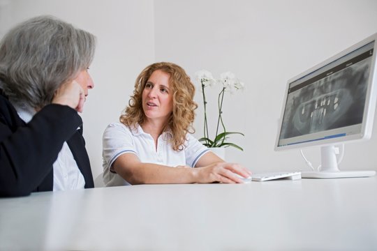 Surface level view of mature woman and senior woman discussing x-ray image on computer screen