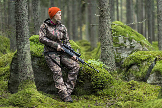 Hunter with rifle sitting on rock in forest
