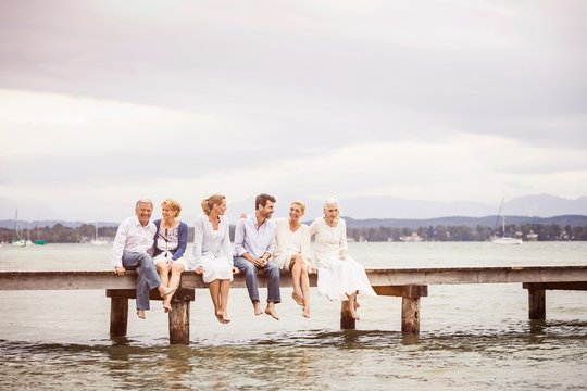 Group of friends, sitting in row on edge of pier