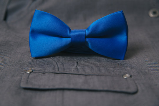 Blue bow tie with wedding rings on textile suit background