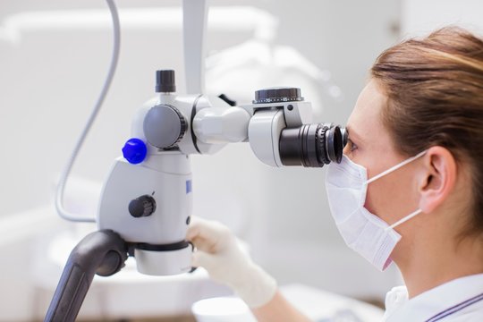 Side view of dentist looking through microscope