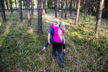 Young child boy giving his sister piggyback outdoors in the forest