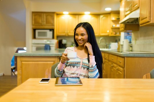 Young woman drinking coffee and using digital tablet  at kitchen table