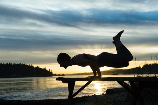 Woman practising yoga by lake at sunset