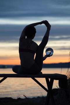 Woman practising yoga by lake at sunset