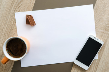 Obraz na płótnie Canvas Desk with white paper, coffee, chocolate and phone on it
