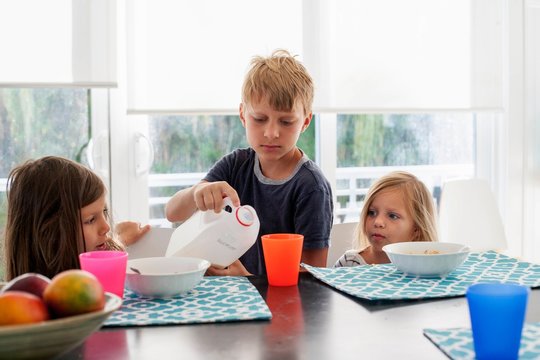 Big brother pouring milk into sisters plastic cup