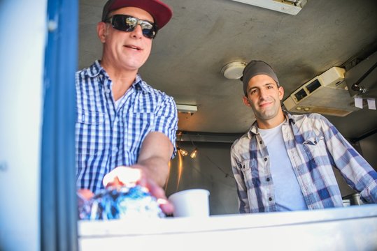 Low angle view of men in catering van looking through hatch at camera smiling