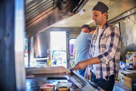 Young man in catering van cooking food on griddle