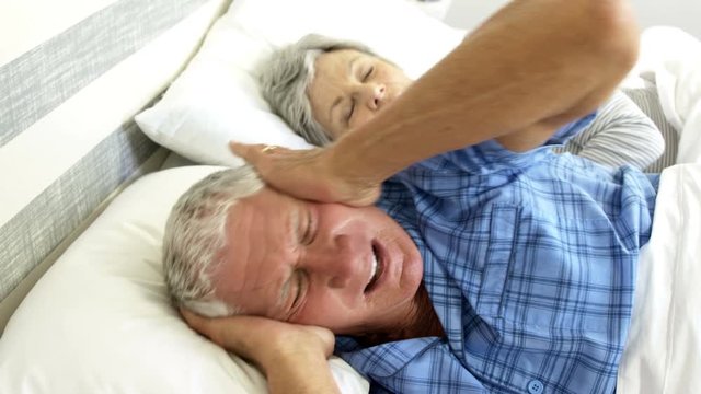 Senior man covering her ears while woman snoring