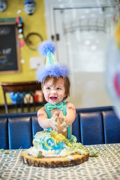 Baby boy wearing party hat smashing first birthday cake at table