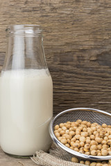 Soybeans and bottle of soy milk, on wooden background.