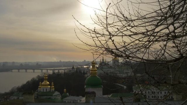 Kiev-Pechersk Lavra View Through Branches Ukraine Sun Shines Through Clouds Dnepr Paton Bridge Through the River Kiev City on a Horizon Sunset Cloudy Sky