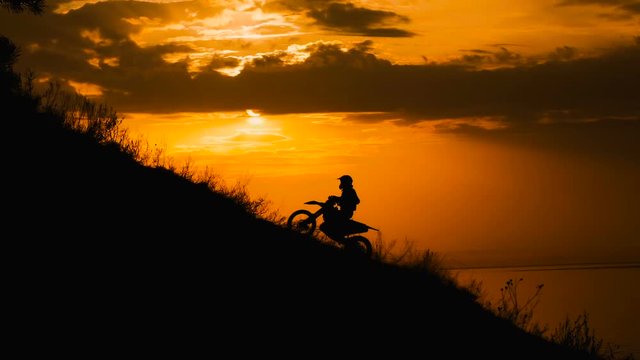 motocross rider storms obstacle. Climb up the hill on the road. Sunset painted the sky 